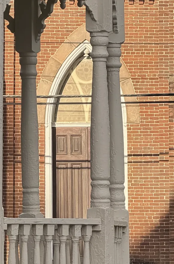 The pointed Gothic doorway of Marion Methodist Church across the street, seen between the turret's turned columns