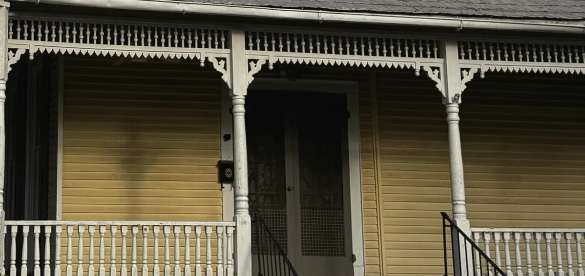 Spindle frieze and gingerbread brackets along the wraparound porch against butter-yellow clapboard