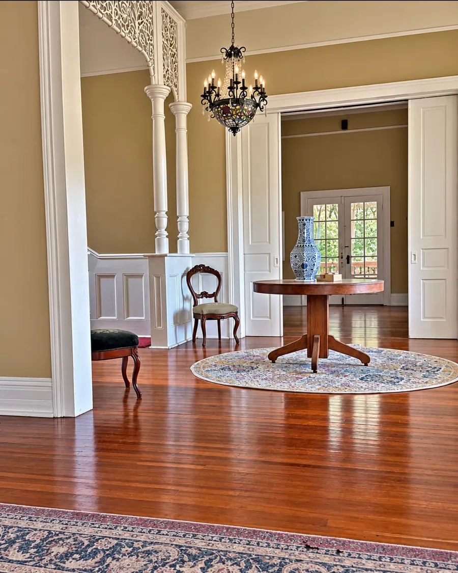 Polished heart-pine floors, a round pedestal table with a blue-and-white vase, and tall pocket doors open to a parlor with French doors